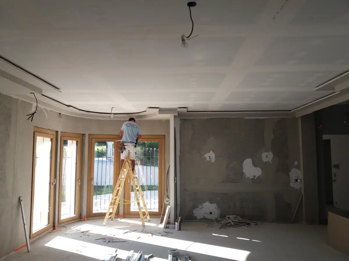 Operaio Fontana Raffaele su una scala mentre completa un controsoffitto in cartongesso con veletta curva lungo le vetrate