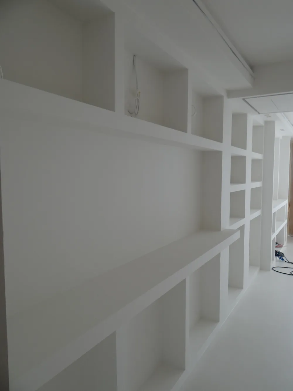 Lunga libreria in cartongesso bianca lungo un corridoio, appena pitturata