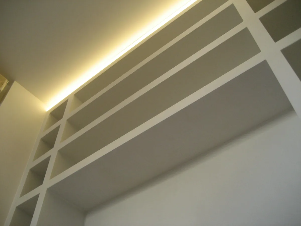 Dettaglio di una libreria in cartongesso illuminata dall'alto da una striscia LED