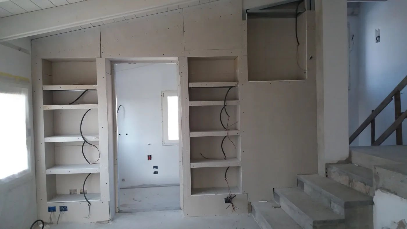 Parete in mansarda con librerie e nicchie in cartongesso appena montate, lastre avvitate e cavi elettrici predisposti